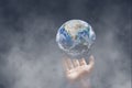 Hand holding blue planet earth in dark room with white smoke. Royalty Free Stock Photo