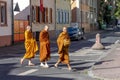 begging monks cross a street in their typical orange dress in the morning with baskets to collect food