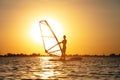 A beginner windsurfer woman stands on a board with a sail on a sunset background. Windsurfing school Royalty Free Stock Photo