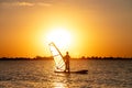 A beginner windsurfer woman stands on a board with a sail on a sunset background. Windsurfing school Royalty Free Stock Photo