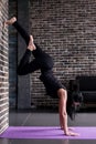 Beginning female yogi practicing yoga inversion poses standing on hands upside down leaning against wall in fitness club