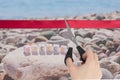 The beginning of the tourist season. Hand cuts a red ribbon with scissors overlooking sea stones pebbles with the inscription