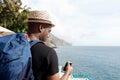 Behind of african american travel man with bag looking at cellphone by the sea Royalty Free Stock Photo