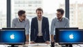 Behind a desk with two computers displaying the Apple logo. They Royalty Free Stock Photo