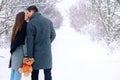 Behind photo of caucasian couple walking in the winter snowy park. Family sweet kiss, holding together a brown plush