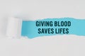 Behind torn white paper on a blue background, the text -GIVING BLOOD SAVES LIFES Royalty Free Stock Photo