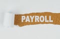 Behind torn white paper on a wooden background the text - PAYROLL