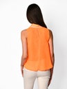 From behind. Young beautiful woman posing in orange shirt and beige pants on a white