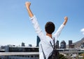 Behind of young woman looking at city with arms raised