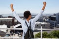 Behind of young woman looking at city with hands raised