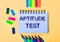 On a beige background, a notebook with the words APTITUDE TEST, bright felt-tip pens and stickers Royalty Free Stock Photo