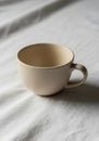 Beige ceramic cup with a rounded shape and a wide handle sits on a white fabric surface, offering a Royalty Free Stock Photo