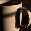 Beige ceramic mug with a curved handle, partially lit by soft, warm sunlight Royalty Free Stock Photo