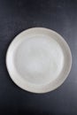 Beige ceramic plate photographed from above on a dark background, vertical format with copy space. Royalty Free Stock Photo