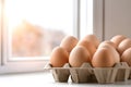 Beige chicken eggs in cardboard packaging on empty table in sunlight from window Royalty Free Stock Photo