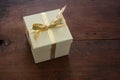 Beige closed gift box with gold color ribbon on wooden table Royalty Free Stock Photo