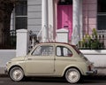 Beige colour vintage Fiat 500 classic car parked in front of a house with a pink door on a street in Notting Hill, Londond UK Royalty Free Stock Photo