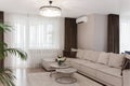 Beige comfortable corner sofa with pillows in elegant living room interior