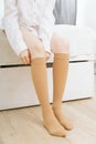 Beige compression stockings on a woman in a white room. Knee socks or socks. Girl putting on stockings at home Royalty Free Stock Photo