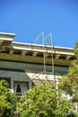 Beige decorative house facade with brown metal fire escape ladder near front yard tree and blue sky background midday Royalty Free Stock Photo