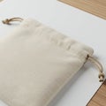 A beige drawstring pouch rests on a white surface with a wooden texture visible in th Royalty Free Stock Photo