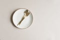 beige empty porcelain plate on pastel background with golden cutlery.