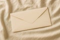 Beige envelope on soft fabric background. Elegant and simple stationery flat lay for mockup or design Royalty Free Stock Photo