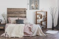 Beige, knit blanket on a pink bed with wooden bedhead in rustic bedroom interior for a woman