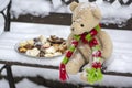 Beige plushy teddy bear with red green striped knitted scarf sitting with Christmas cookies on the bench covered with white snow Royalty Free Stock Photo