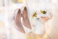 beige shoes for bride hanging on a white chair against a background of a bouquet of pions