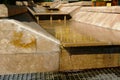 Beige stone cladded fountain in the summer with trickeling water stream. abstract view.