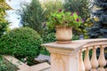 A beige stone flowerpot with blooming flowers on the railing.