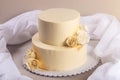 Beige 2 tiered wedding cake decorated with mastic roses stands on fabric background Royalty Free Stock Photo
