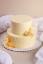 Beige 2 tiered wedding cake decorated with mastic roses stands on fabric background Royalty Free Stock Photo