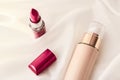 Beige tonal cream bottle make-up fluid foundation base and red lipstick on silk background, cosmetics products as luxury beauty