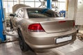 Beige used car with an open hood raised on a lift for repairing the chassis and engine in a vehicle repair shop. Auto service