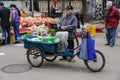 Old lady sells celery off blue tricycle on market.