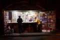 CLOSE UP: Three local men stand idle at a newspaper stand in the middle of night