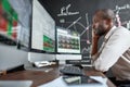 Being late. Portrait of stylish african businessman, trader sitting by desk in front of multiple monitors. He is getting