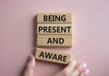 Being Present and Aware symbol. Wooden blocks with words Being Present and Aware. Doctor hand. Beautiful pink background.