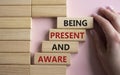 Being Present and Aware symbol. Wooden blocks with words Being Present and Aware. Doctor hand. Beautiful pink background.