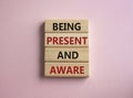 Being Present and Aware symbol. Wooden blocks with words Being Present and Aware. Doctor hand. Beautiful pink background.