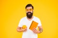 Being proud of geek in you. Geek man. Bearded man in geek glasses holding orange and book on yellow background. Hipster