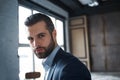 Being successful. Close-up portrait of bearded young businessman who is looking at camera while standing in office