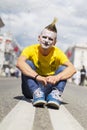 The punk guy in bright clothes sitting on the street