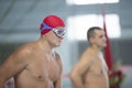 A male swimmer in a swimming cap and goggles on the background of the pool