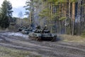 Russian armored combat vehicles are navigating through marshland through forests. Tankmen on the T-90