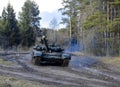 Russian armored combat vehicles are navigating through marshland through forests. Tankmen on the T-90