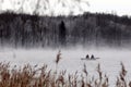 BELARUS - November 2010: Fishermen on a boat on the lake during the fog against the background of dark trees. Royalty Free Stock Photo