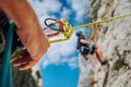 Belay device close-up shot with a boy on the cliff climbing wall. He hanging on a rope in a climbing harness and his partner